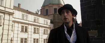 Movie still from “The Brothers Bloom” (2008), directed by Rian Johnson – A man wearing a black hat standing in front of a building; Close Up shot, Low angle