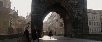 Movie still from “The Brothers Bloom” (2008), directed by Rian Johnson – A woman is walking under an archway on a street; Extreme Wide shot, High angle