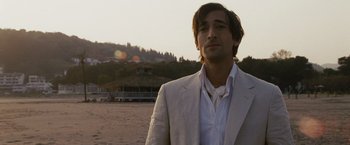 Movie still from “The Brothers Bloom” (2008), directed by Rian Johnson – A man wearing a suit standing on the beach; Close Up shot, Over the shoulder angle