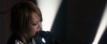 Movie still from “The Brothers Bloom” (2008), directed by Rian Johnson – A woman singing into a microphone in front of a spotlight; Close Up shot, Low angle