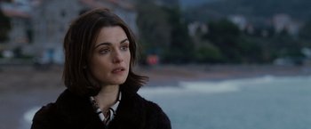 Movie still from “The Brothers Bloom” (2008), directed by Rian Johnson – A person wearing a jacket near a body of water; Close Up shot, Over the shoulder angle