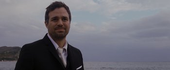 Movie still from “The Brothers Bloom” (2008), directed by Rian Johnson – A person wearing a suit near the ocean; Close Up shot, Over the shoulder angle