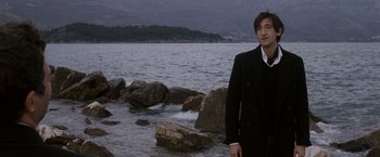 Movie still from “The Brothers Bloom” (2008), directed by Rian Johnson – A man standing in the water near some rocks; Medium shot, Over the shoulder angle