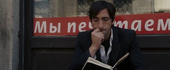 Movie still from “The Brothers Bloom” (2008), directed by Rian Johnson – A man in a black suit is reading a book; Close Up shot, High angle