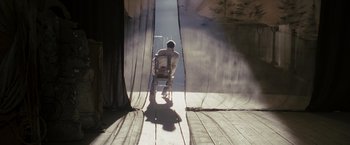 Movie still from “The Brothers Bloom” (2008), directed by Rian Johnson – A man sitting on a chair in a room; Wide shot, High angle