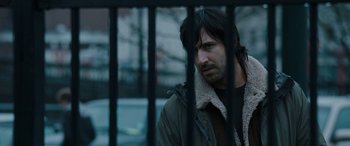Movie still from “The Burning Plain” (2008), directed by Guillermo Arriaga – A man standing behind a metal fence looking at the camera; Close Up shot, Over the shoulder angle