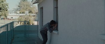 Movie still from “The Burning Plain” (2008), directed by Guillermo Arriaga – A man leaning against a wall looking into a window; Medium shot, High angle