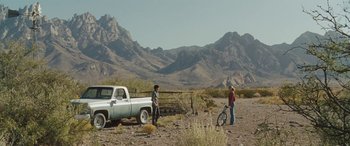 Movie still from “The Burning Plain” (2008), directed by Guillermo Arriaga – Two people standing in front of a truck and a bicycle; Extreme Wide shot, Over the shoulder angle