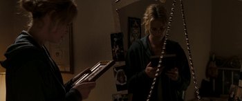 Movie still from “The Burning Plain” (2008), directed by Guillermo Arriaga – A woman looking at her cell phone while a man plays a guitar; Medium shot, High angle