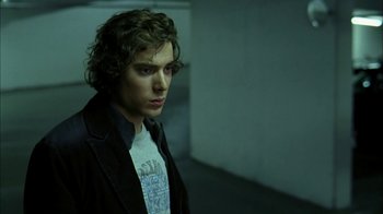 Movie still from “The Butterfly Effect 2” (2006), directed by John R. Leonetti – A young man in a black jacket is standing in a dark room; Close Up shot, Over the shoulder angle