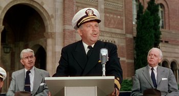Movie still from “The Caine Mutiny” (1954), directed by Edward Dmytryk – A man in a naval uniform is speaking at a podium; Medium shot, Low angle