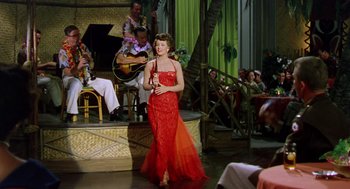 Movie still from “The Caine Mutiny” (1954), directed by Edward Dmytryk – A woman in a long red dress holding a violin; Wide shot, Low angle