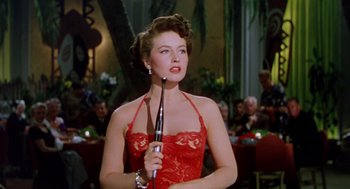 Movie still from “The Caine Mutiny” (1954), directed by Edward Dmytryk – A woman in a red dress holding a microphone in her hand; Medium shot, Low angle