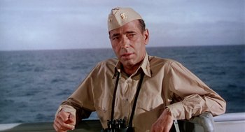 Movie still from “The Caine Mutiny” (1954), directed by Edward Dmytryk – A man wearing a hat sitting in front of a body of water with binoculars; Close Up shot, Low angle
