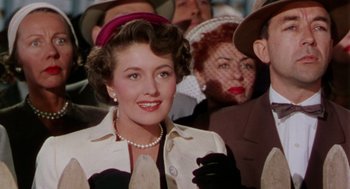Movie still from “The Caine Mutiny” (1954), directed by Edward Dmytryk – A woman in a crowd of people wearing a hat and gloves; Close Up shot, Low angle