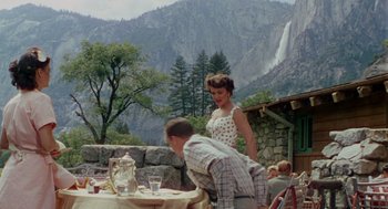 Movie still from “The Caine Mutiny” (1954), directed by Edward Dmytryk – A man and a woman standing at an outdoor table with mountains in the background; Extreme Wide shot, High angle