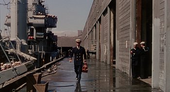 Movie still from “The Caine Mutiny” (1954), directed by Edward Dmytryk – A man in uniform walking down a wet street; Wide shot, High angle