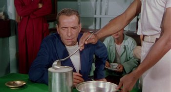 Movie still from “The Caine Mutiny” (1954), directed by Edward Dmytryk – A man sitting at a table with a spoon in his mouth; Medium shot, High angle
