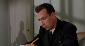 Movie still from “The Caine Mutiny” (1954), directed by Edward Dmytryk – A man in a suit writing on a piece of paper with a pencil; Close Up shot, High angle