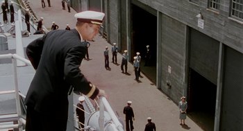 Movie still from “The Caine Mutiny” (1954), directed by Edward Dmytryk – A man in a uniform standing next to a boat; Wide shot, High angle