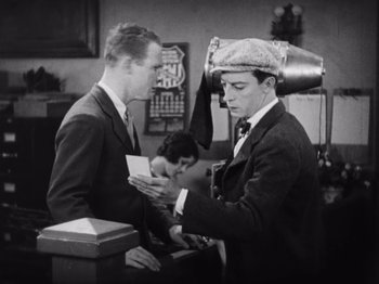 Movie still from “The Cameraman” (1928), directed by Buster Keaton – Two men in suits and hats are looking at papers; Medium shot, High angle
