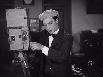 Movie still from “The Cameraman” (1928), directed by Buster Keaton – A man in a suit and hat is painting a picture; Medium shot, Low angle