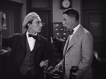 Movie still from “The Cameraman” (1928), directed by Buster Keaton – Two men in suits talking to each other in an office setting; Medium shot, Low angle