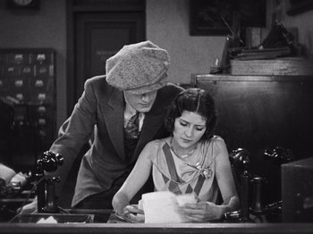 Movie still from “The Cameraman” (1928), directed by Buster Keaton – A man and a woman sitting at a desk; Medium shot, High angle