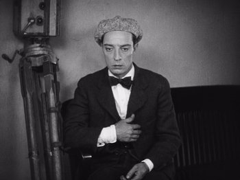 Movie still from “The Cameraman” (1928), directed by Buster Keaton – A black and white photo of a man wearing a suit and hat; Medium shot, High angle