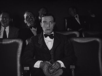 Movie still from “The Cameraman” (1928), directed by Buster Keaton – A man sitting in a chair in front of two other men; Medium shot, Low angle