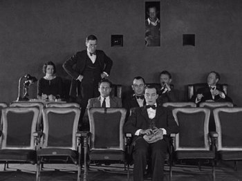 Movie still from “The Cameraman” (1928), directed by Buster Keaton – A group of people sitting in a room; Wide shot, High angle