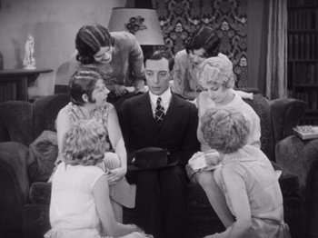 Movie still from “The Cameraman” (1928), directed by Buster Keaton – A group of people sitting around a man in a suit; Medium shot, High angle