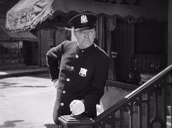 Movie still from “The Cameraman” (1928), directed by Buster Keaton – A man in a police uniform leaning on a railing in front of a building; Medium shot, Low angle