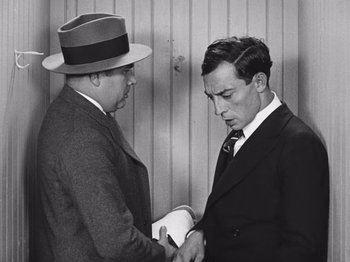 Movie still from “The Cameraman” (1928), directed by Buster Keaton – Two men in suits and hats are shaking hands; Medium shot, Low angle