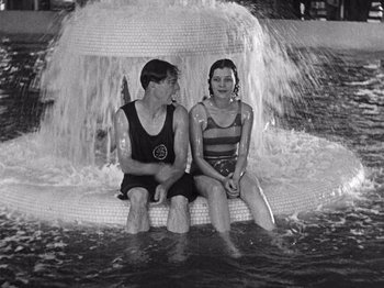 Movie still from “The Cameraman” (1928), directed by Buster Keaton – A man and a woman sitting on a chair in the water; Medium shot, High angle