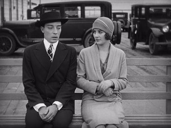 Movie still from “The Cameraman” (1928), directed by Buster Keaton – A man and a woman sitting on a bench in front of a car; Medium shot, High angle