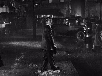 Movie still from “The Cameraman” (1928), directed by Buster Keaton – A black and white photo of a man walking in the rain; Wide shot, High angle