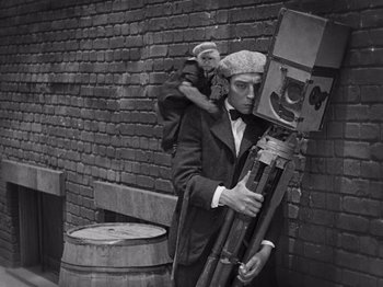 Movie still from “The Cameraman” (1928), directed by Buster Keaton – A man in a suit and hat holding a camera; Medium shot, Low angle