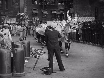 Movie still from “The Cameraman” (1928), directed by Buster Keaton – An old photo of a man holding an umbrella in the street; Wide shot, Low angle