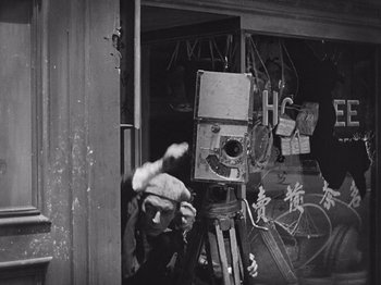 Movie still from “The Cameraman” (1928), directed by Buster Keaton – An old photo of a person with a camera in front of a building; Medium shot, Low angle