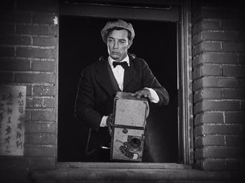 Movie still from “The Cameraman” (1928), directed by Buster Keaton – A black and white photo of a man holding a camera; Medium shot, Low angle