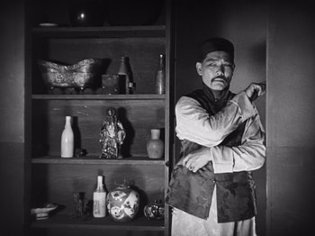Movie still from “The Cameraman” (1928), directed by Buster Keaton – A man standing in front of a book shelf; Medium shot, Low angle