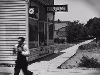 Movie still from “The Cameraman” (1928), directed by Buster Keaton – A man walking down the street in front of a drug store; Extreme Wide shot, Low angle
