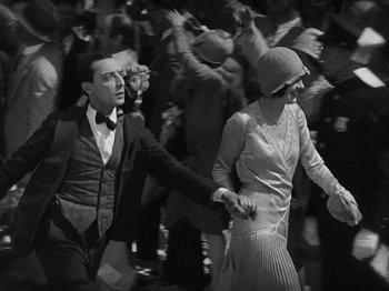 Movie still from “The Cameraman” (1928), directed by Buster Keaton – A man and a woman are holding hands in front of a crowd of onlookers; Medium shot, High angle