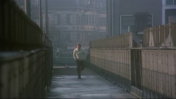 Movie still from “The Cassandra Crossing” (1976), directed by George P. Cosmatos – A woman walking down a sidewalk on a foggy day; Wide shot, Low angle