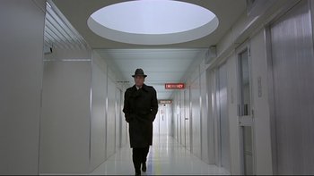 Movie still from “The Cassandra Crossing” (1976), directed by George P. Cosmatos – A man in a black coat and hat walking down a hall way; Wide shot, Low angle