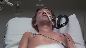 Movie still from “The Cassandra Crossing” (1976), directed by George P. Cosmatos – A man laying on a hospital bed with an electrical device attached to his face; Close Up shot, Overhead angle