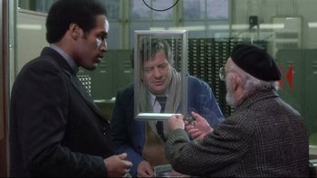 Movie still from “The Cassandra Crossing” (1976), directed by George P. Cosmatos – Two men and a man in a suit looking at a man in a mirror; Medium shot, Over the shoulder angle