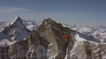 Movie still from “The Cassandra Crossing” (1976), directed by George P. Cosmatos – A red helicopter flying over a snowy mountain top; Extreme Wide shot, High angle