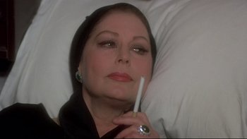 Movie still from “The Cassandra Crossing” (1976), directed by George P. Cosmatos – An older woman laying in bed with a cigarette in her mouth; Close Up shot, High angle